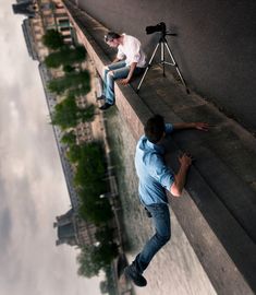 two men are sitting on the edge of a wall and one man is holding a camera