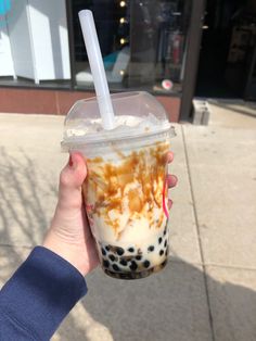 a person holding up a cup with ice cream and caramel on it in front of a building