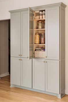 an open cabinet in the middle of a room with wood flooring and white walls