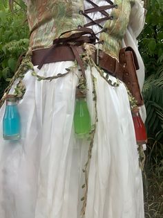 Green corset over white dress with hanging potions Potion Seller Costume, Ren Faire Fairy Accessories, Ren Faire Outfits Accessories, Fantasy Apothecary Outfit, Green Fairy Ren Faire, Ren Fair Elf Costume, Ren Faire Corset Outfit, Trinket Fairy Costume, Ren Faire Goblin