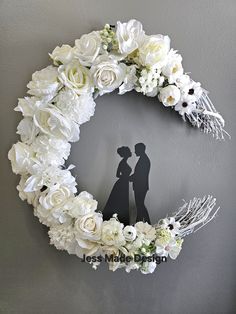 the silhouette of a bride and groom in front of a white flower wreath on a gray wall