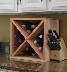 a wooden wine rack with bottles and knives in it on a kitchen counter next to white cabinets