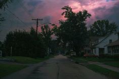 the sky is pink and purple as the sun goes down on a residential street lined with houses