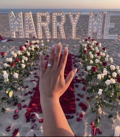 someone's hand in front of a beach with roses and letters that spell out marry me