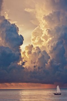 a sailboat sailing on the ocean under a cloudy sky with sunbeams in the distance