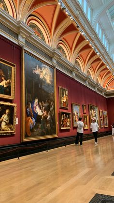 people looking at paintings on display in a museum with red walls and white ceilinging