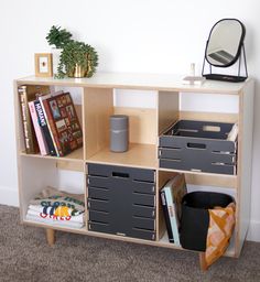 a book shelf with bins, books and other items on it next to a mirror