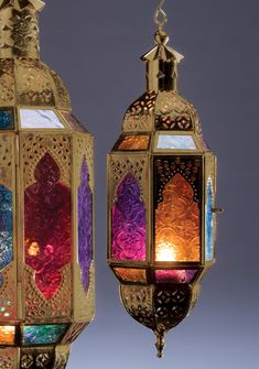 two colorful lanterns hanging from the ceiling in front of a gray background, one with an intricate design on it