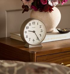 a white clock sitting on top of a wooden table next to a vase filled with flowers