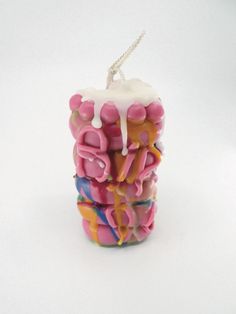 a candle that has been decorated with pink and yellow icing on the top, sitting in front of a white background