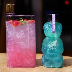 two plastic bottles with different colored liquids in them on a wooden table top, one is filled with ice and the other has a strawberries