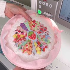 a person is holding a decorative item in front of a machine that has buttons on it