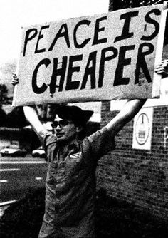 a man holding up a sign that says peace is cheaper