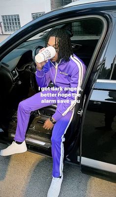 a man sitting in the door of a car drinking from a bottle while wearing purple tracksuits