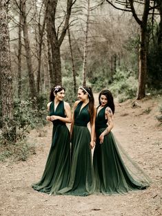 three bridesmaids in green dresses standing together on a dirt path surrounded by trees