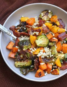 a white bowl filled with vegetables and rice on top of a brown table cloth next to a fork