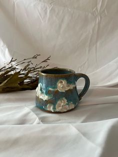 a blue mug with white flowers on it sitting next to a twig and dried plant