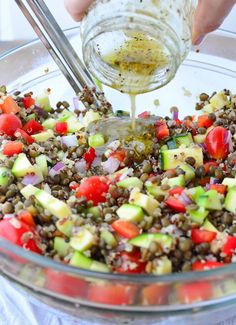 someone is adding dressing to a salad in a glass bowl on a white tablecloth