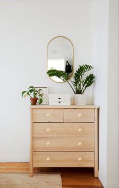 a bedroom with a dresser, mirror and potted plants