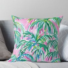 a pink and green palm tree print pillow on a gray couch with white throw pillows