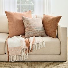 a couch with pillows and blankets on it in front of a window, next to a rug