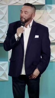 a man standing in front of a microphone with his hand on his hip and wearing a suit