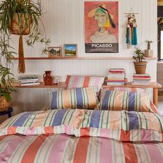 a bed with striped sheets and pillows in a bedroom next to a plant on the wall