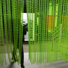 an artistic installation with green and orange chains hanging from the ceiling