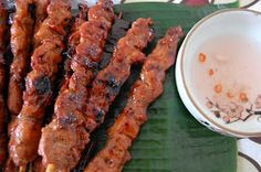 several skewers of meat sitting on a green tray next to a white bowl