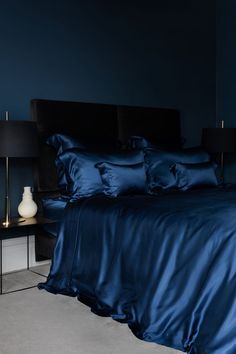 a bed with blue sheets and pillows in a dark room next to a night stand