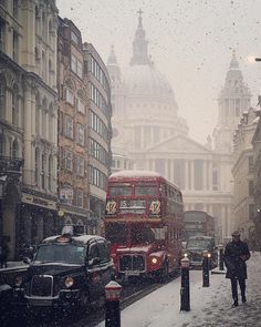 a double decker bus driving down a street next to tall buildings in the snow with traffic passing by