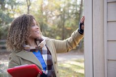 a woman holding a clipboard and looking at something on the wall in front of her