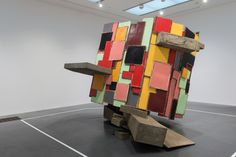 a sculpture made out of different colored blocks on top of a black floor next to a white wall