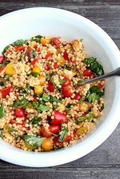 a white bowl filled with grains and vegetables on top of a wooden table next to a fork