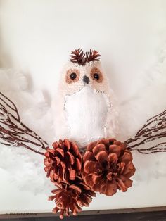 an owl is sitting on top of some pine cones and branches in front of a white background