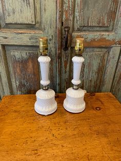 two white candlesticks sitting on top of a wooden table next to an old door