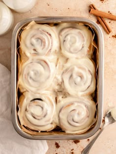 a pan filled with cinnamon rolls on top of a table next to some cinnamon sticks