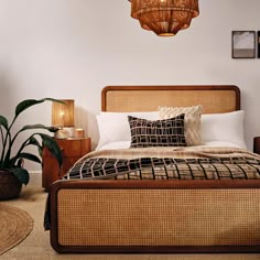 a bed with wicker headboard and pillows in a white room next to a lamp