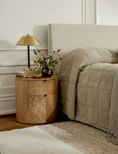 a bed sitting next to a night stand on top of a wooden floor