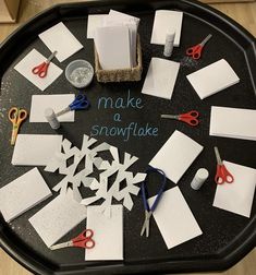 a black tray topped with lots of cut out snowflakes next to scissors and paper