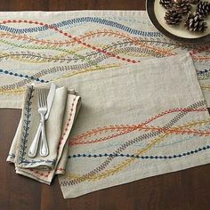 two place mats with forks and spoons sitting on top of each other next to pine cones