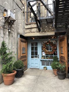 an old building with potted plants in front of the door and lights above it