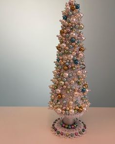 a small white christmas tree with ornaments on it's top and bottom, in front of a gray background