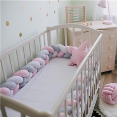 a white crib with pink and grey pillows on it