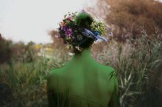 a woman with flowers in her hair standing in tall grass and looking into the distance