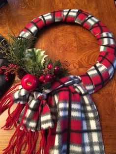 a plaid christmas wreath with red berries and greenery on the top, sitting on a wooden table