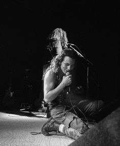 a man sitting on the ground with a microphone in his hand and another person standing behind him