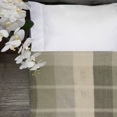 a bed with white flowers on top of it next to a plaid blanket and pillow