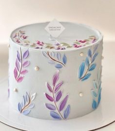 a white cake with purple and blue flowers painted on the top is sitting on a plate