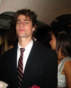 a young man in a suit and tie standing next to other people at a party